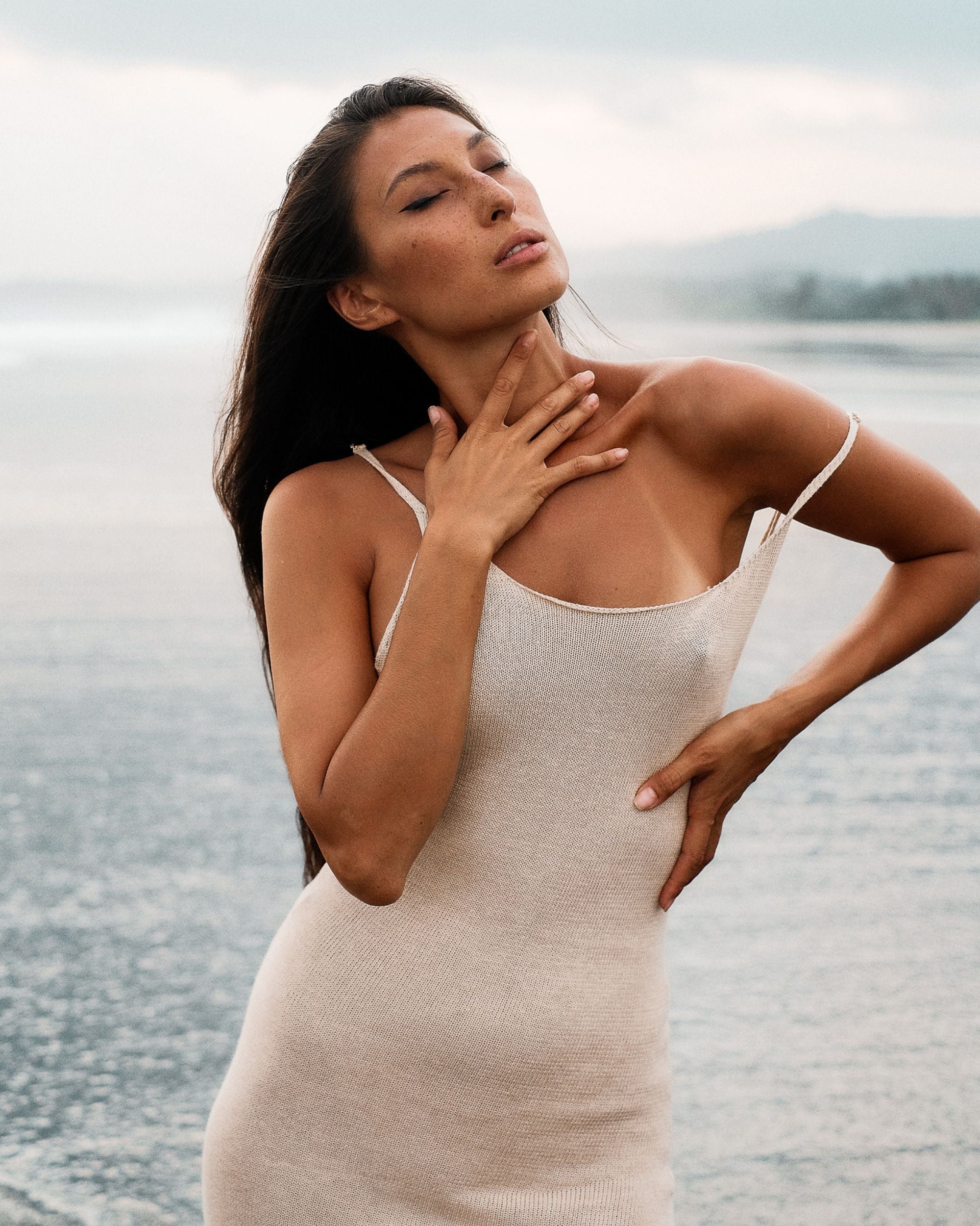 Woman in a beige dress standing by a body of water