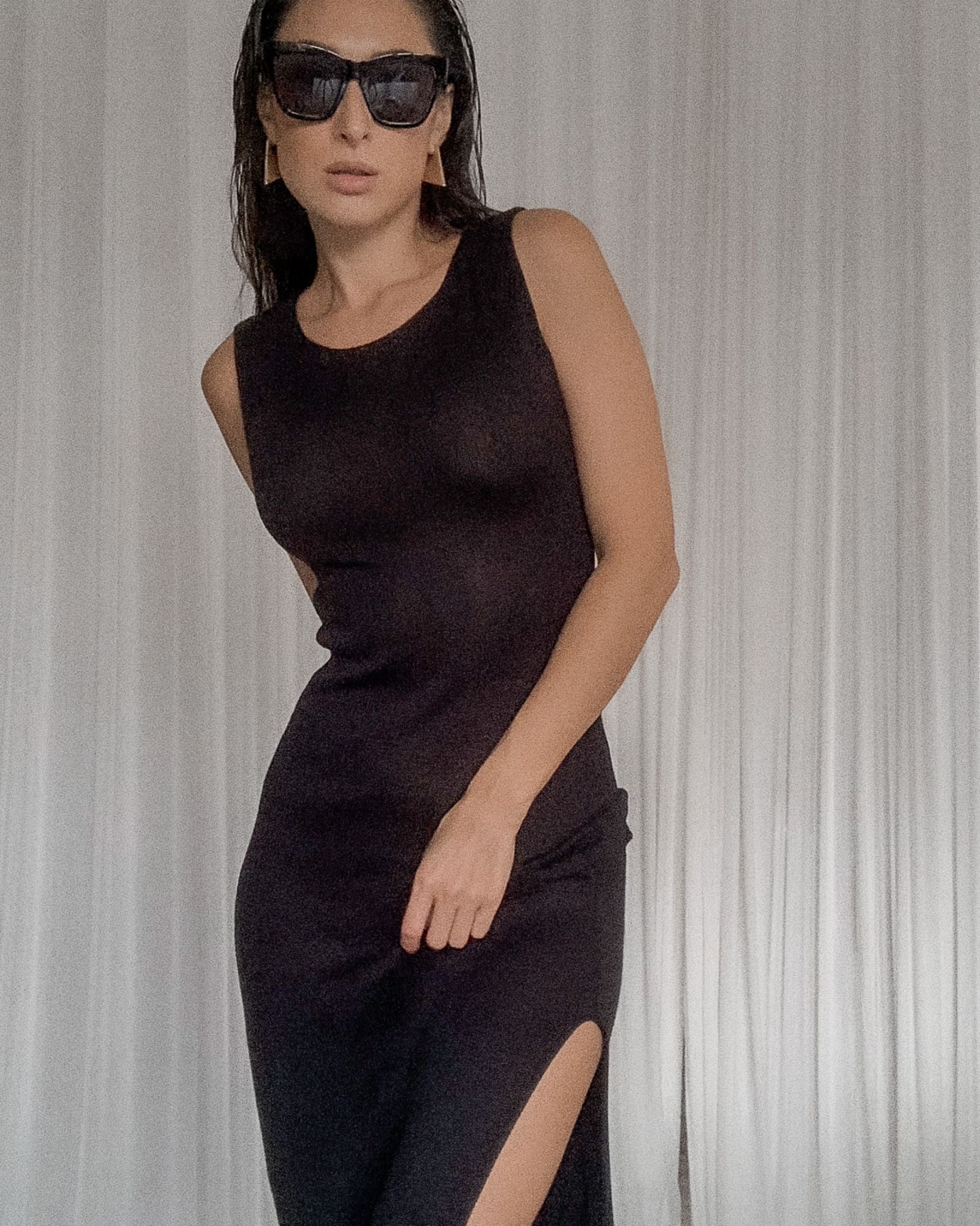 Woman wearing a black sleeveless dress with a slit, standing against a neutral background.