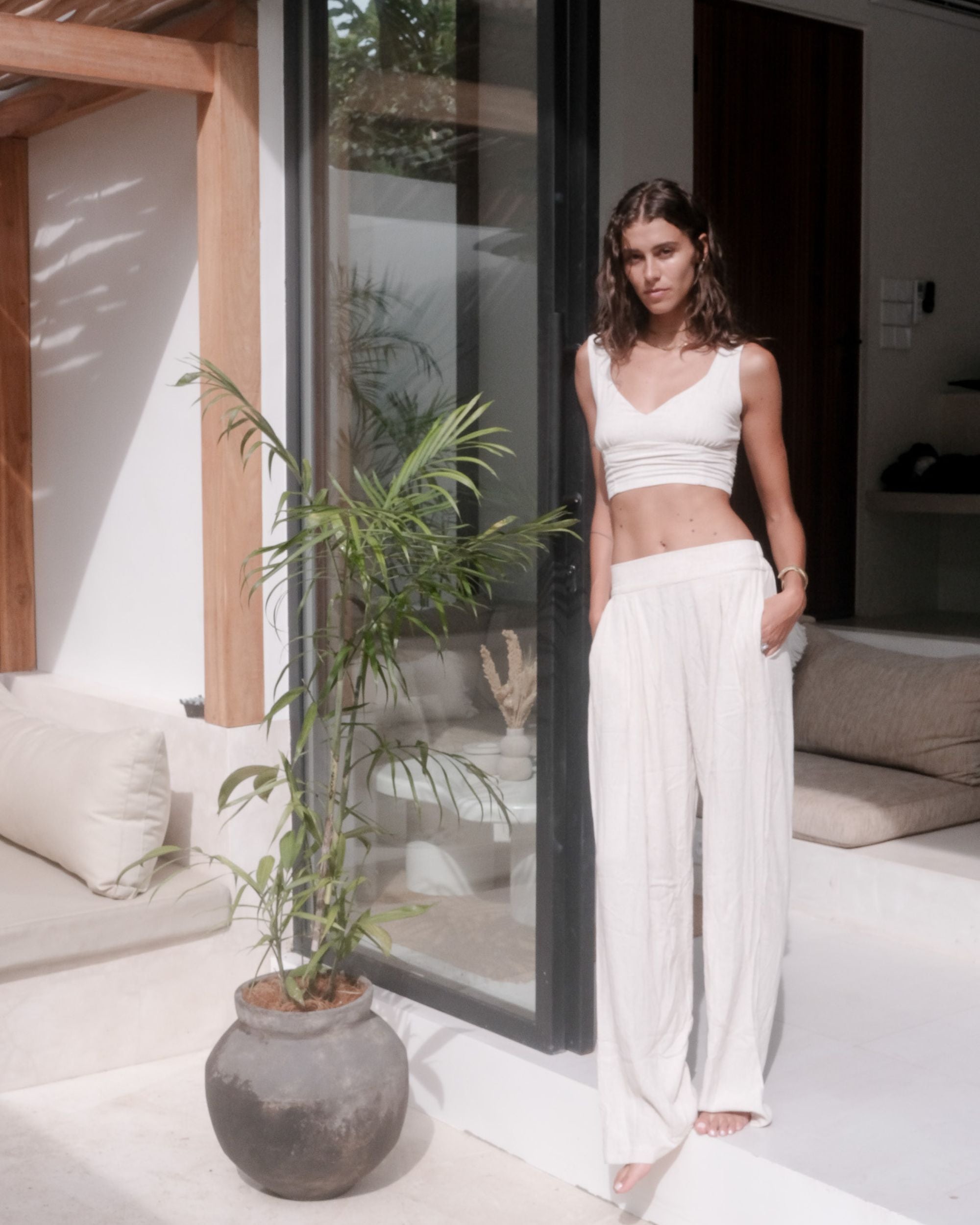 Woman in a white outfit standing in a modern indoor setting with a plant nearby.